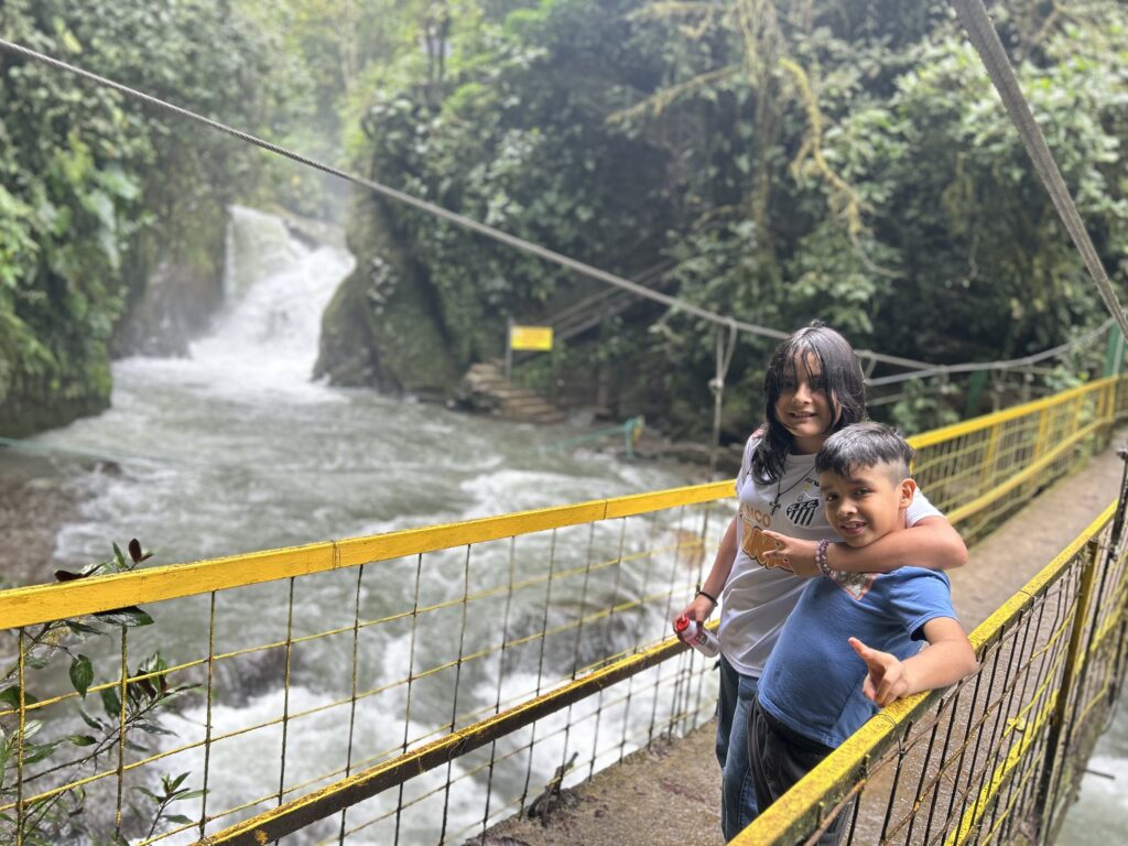 Dos niños en el puente sobre el río, con la cascada al fondo