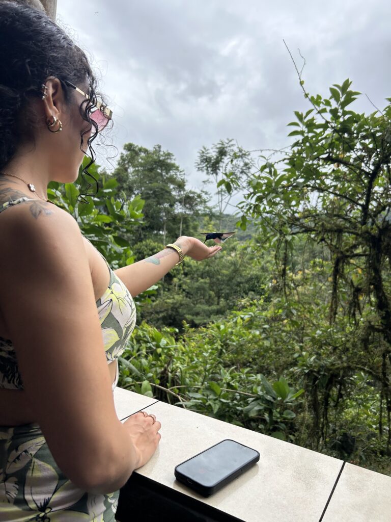 Visitante con un colibrí posado en su dedo frente al bosque nublado