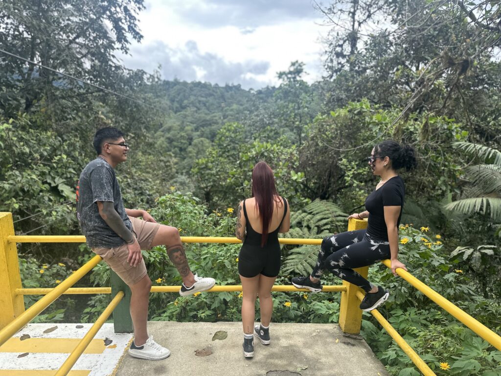 Tres visitantes conversando en un mirador sobre el bosque nublado
