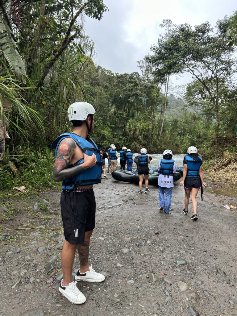 Guía y grupo con chalecos y cascos bajando al río para hacer tubing en Mindo