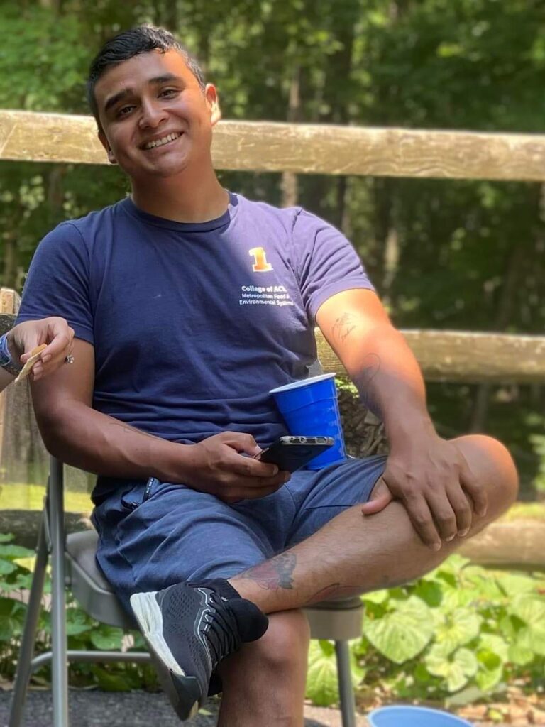 Brandon Minga sonriendo, sentado junto a una baranda de madera en el bosque