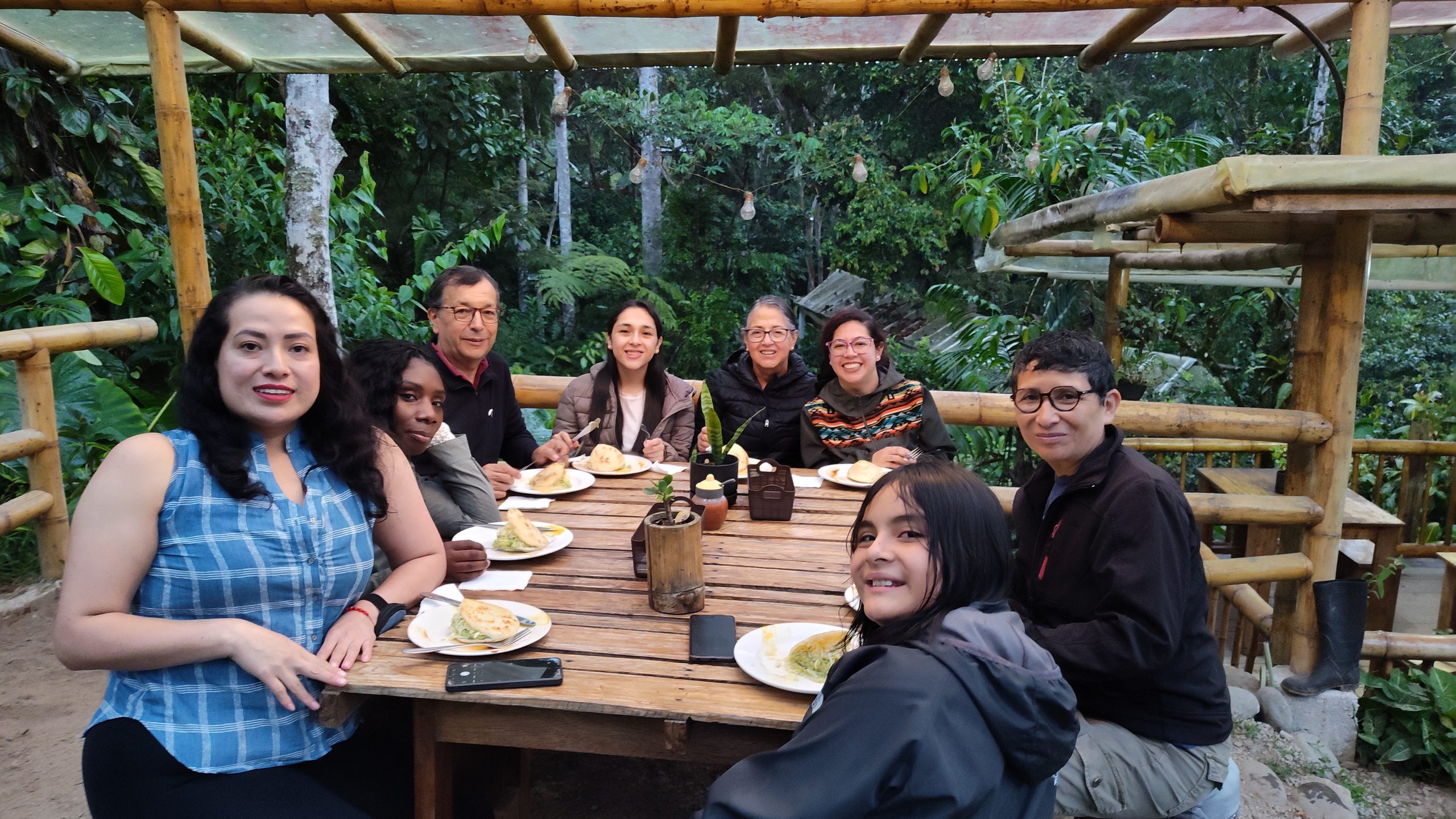 Grupo de visitantes compartiendo la comida en una mesa al aire libre rodeada de bosque en Mindo